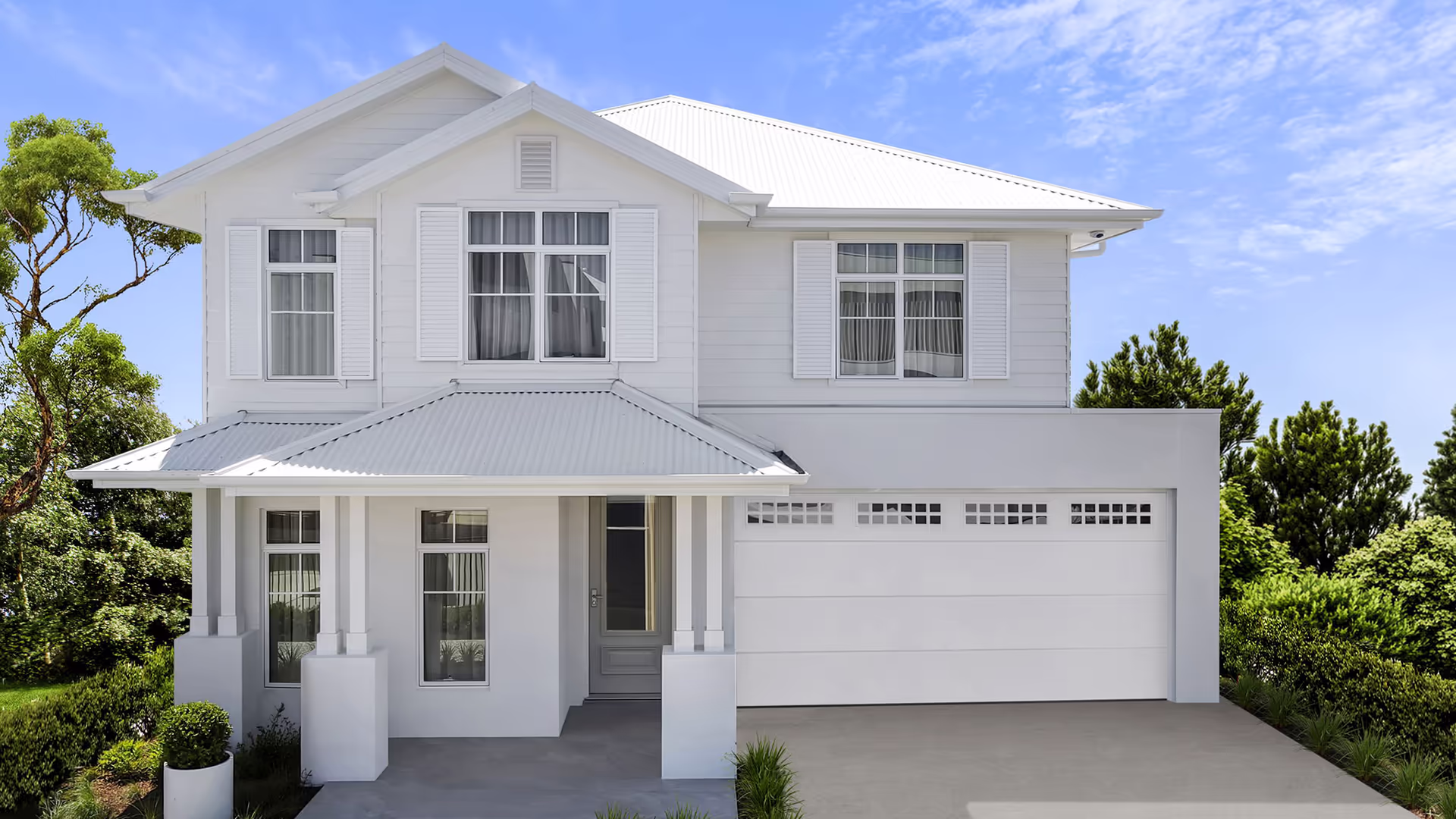 Two-story modern white house with large windows, a double garage, and a covered front porch, surrounded by greenery under a clear blue sky.
